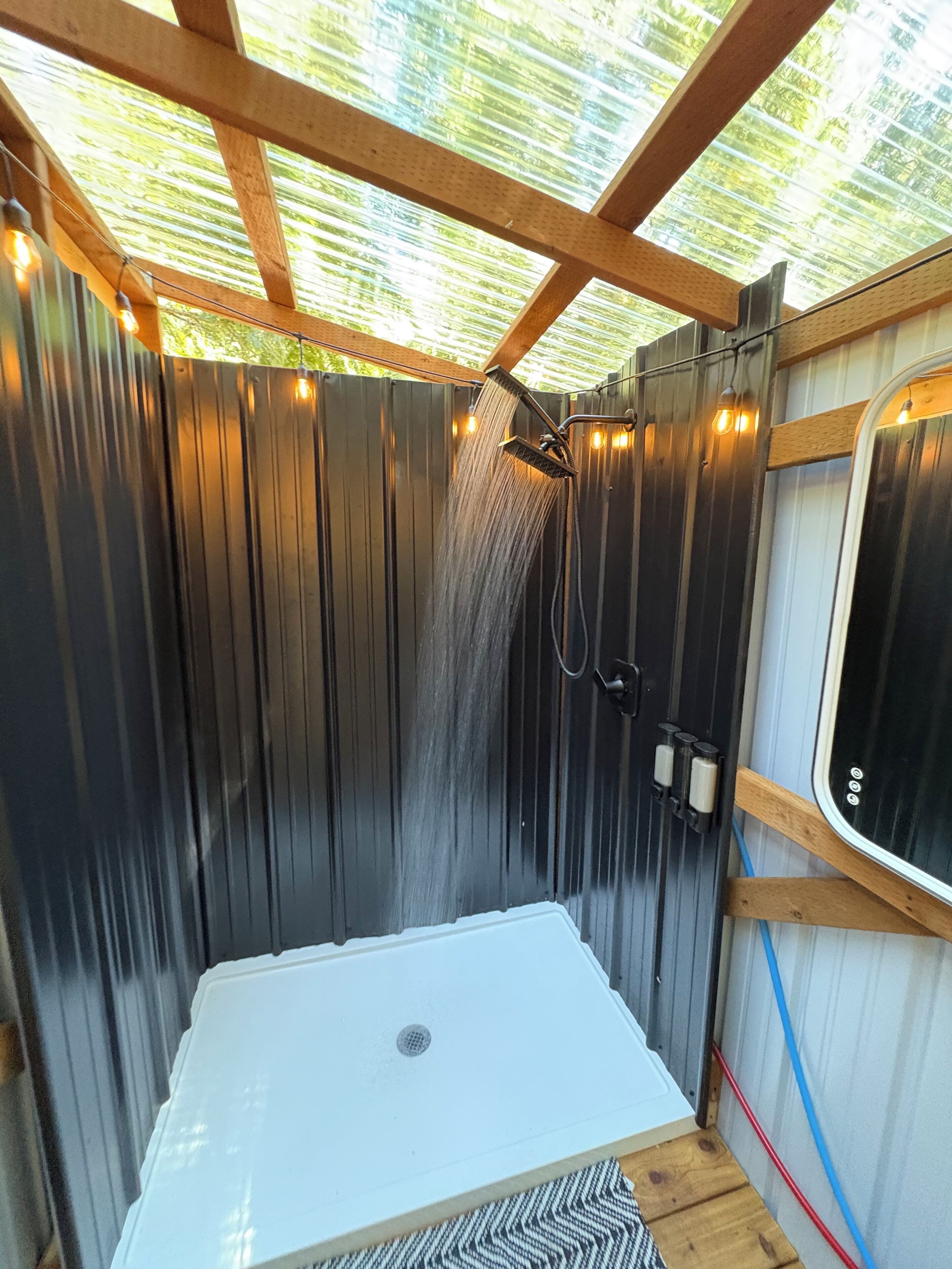 A shower area with a wooden ceiling and metal walls, a white bathtub, and a window with a view of greenery.