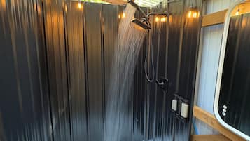 A shower area with a wooden ceiling and metal walls, a white bathtub, and a window with a view of greenery.