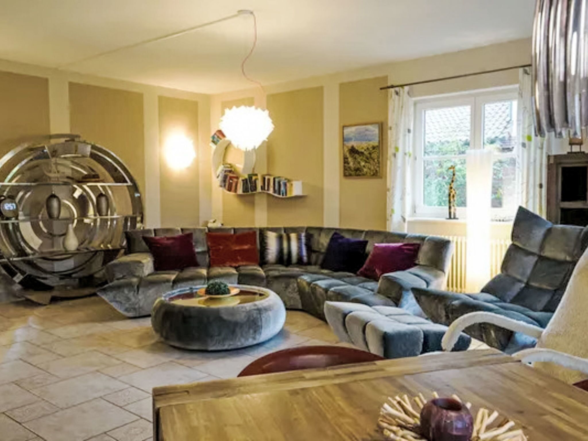 Uma sala de estar com um sofá seccional, uma mesa de centro redonda e uma grande escultura decorativa de metal.