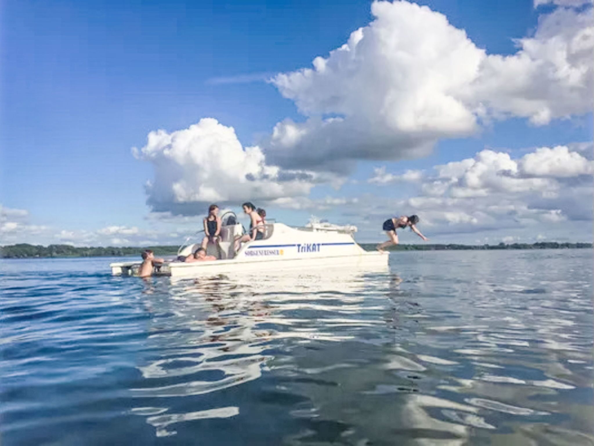Een boot met mensen, drijvend op het water onder een heldere lucht met wolken.