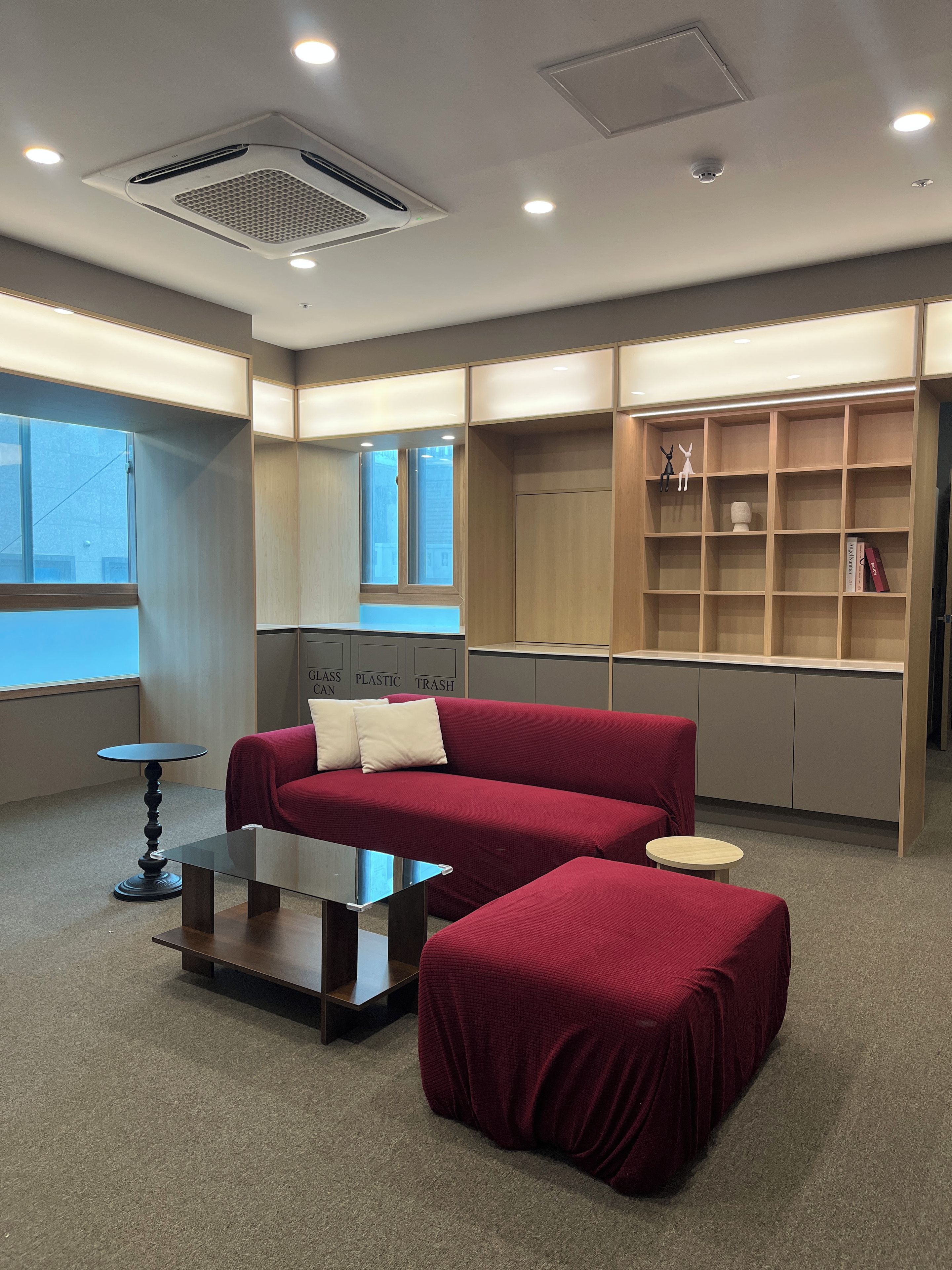 Un interior moderno con un sofá rojo, una mesa de centro de vidrio y una estantería de madera.