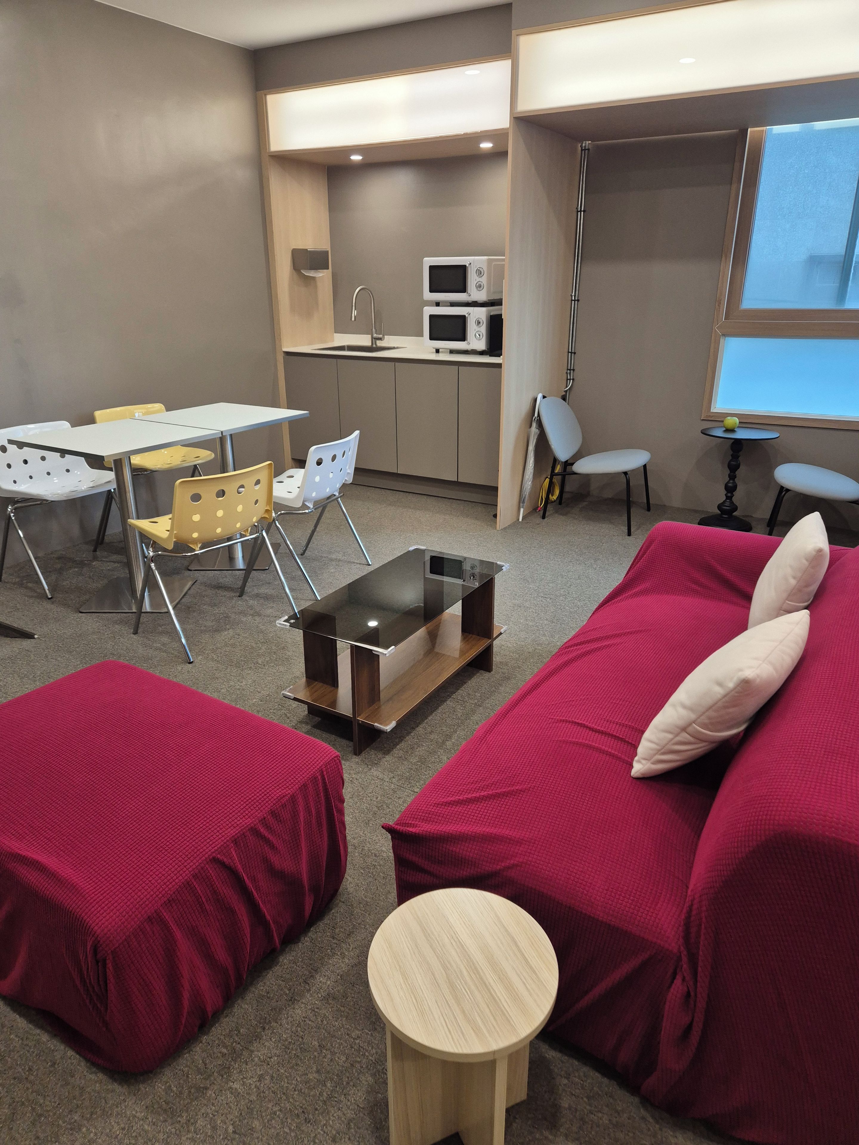 Un espacio habitable compacto con kitchenette, una zona de comedor con sillas, un sofá con cojines y una pequeña mesa redonda.