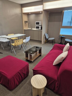 A compact living space with a kitchenette, a dining area with chairs, a sofa with cushions, and a small round table.