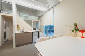 A modern office space with a white conference table, a kitchenette, a microwave, and a view of the outside through a large window. - MONTHLIV Konkuk Univ. Seongsu Hotel Stay (Seoul)