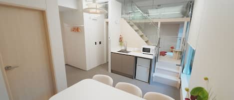 Une cuisine moderne équipée d’un four à micro-ondes, d’un évier et d’un petit réfrigérateur. On y trouve également un coin repas avec une table et des chaises, ainsi qu’un escalier menant à l’étage supérieur.