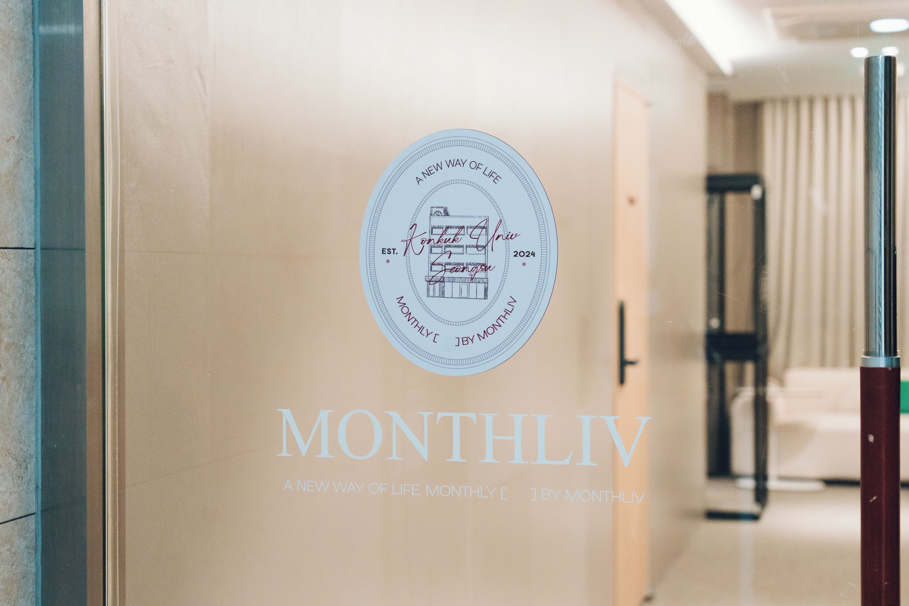 En væg med et cirkulært emblem, der viser en illustration af en bygning og teksten 'MONTHLIV' nedenunder.