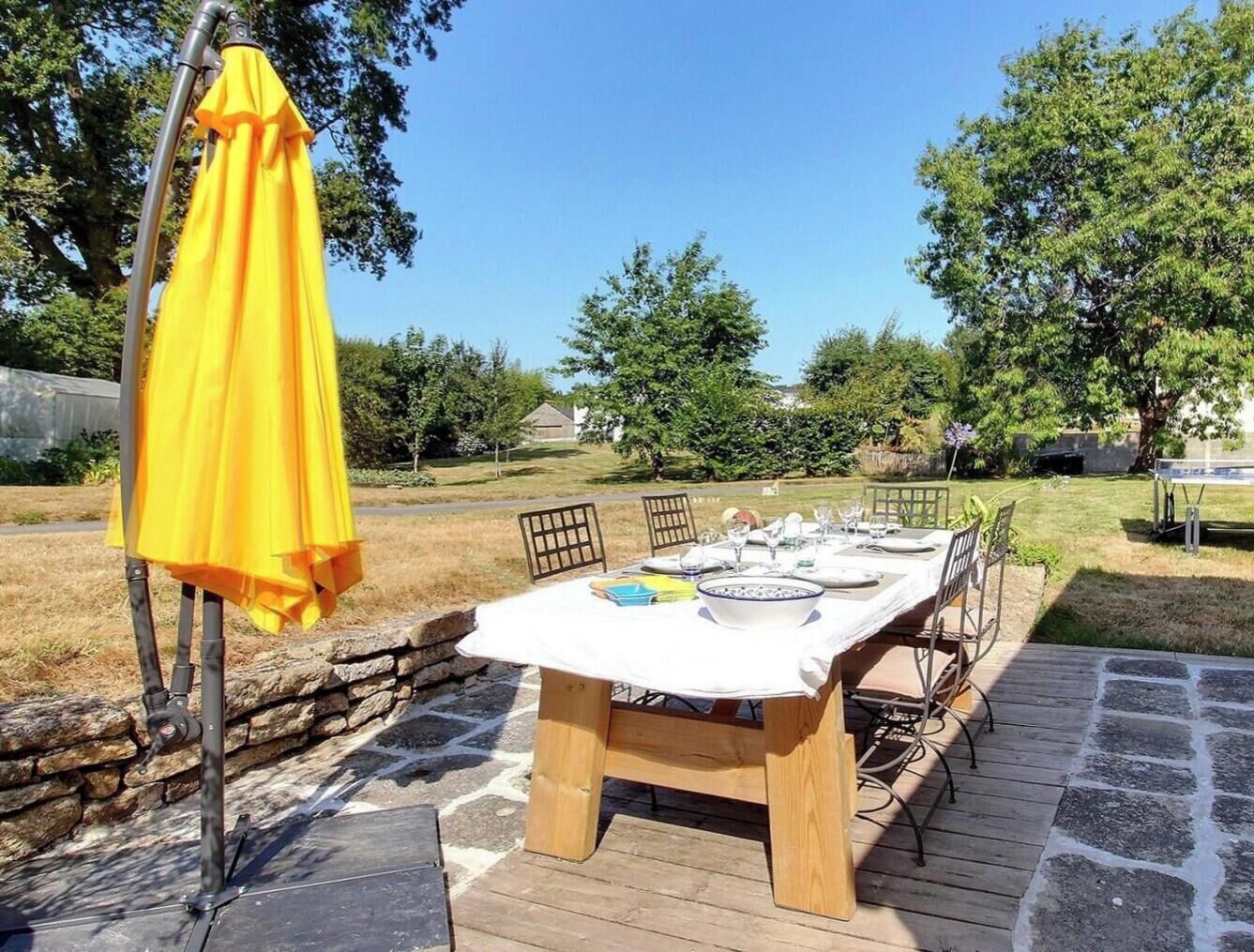 An outdoor dining area with a table set for four, surrounded by chairs, under a yellow umbrella.