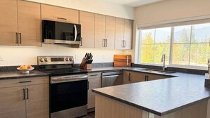 Una cocina moderna con electrodomésticos integrados, armarios de madera y un amplio ventanal con vistas a árboles.