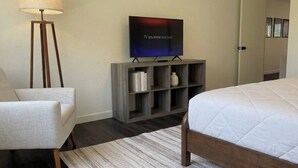 Habitación de hotel con cama, una silla, un televisor sobre un soporte de madera y una estantería.
