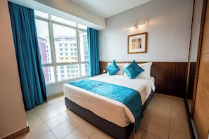 A hotel room with a large bed, a window with curtains, a framed picture on the wall, and a wooden headboard.