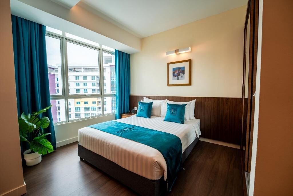 Habitación de hotel con una cama grande, una planta en maceta, una ventana con cortinas e imagen enmarcadas en la pared.