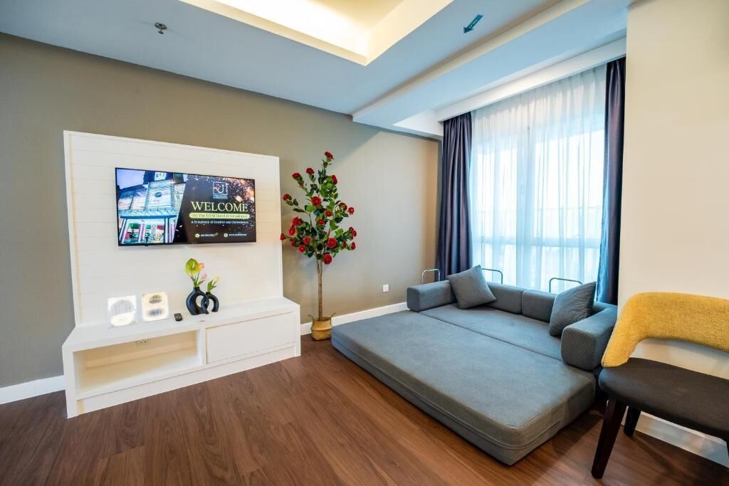 A modern living room with a flat-screen TV mounted on a white console, a grey sofa, and a potted red flower plant.