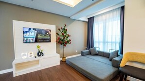 A modern living room with a flat-screen TV mounted on a white console, a grey sofa, and a potted red flower plant. - Utm Hotel Residence (Kuala Lumpur)