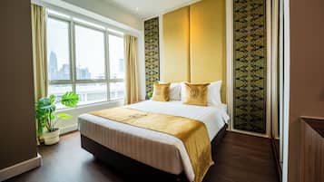 A hotel room with a large bed, a window with curtains, a potted plant, and a view of the city skyline.