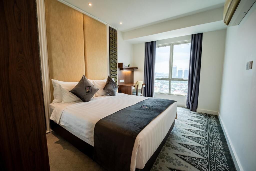 A hotel room with a large bed, a view of the city, and a patterned carpet.