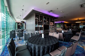 A modern library with a large bookshelf, round tables, and chairs, and a view of the city through large windows.