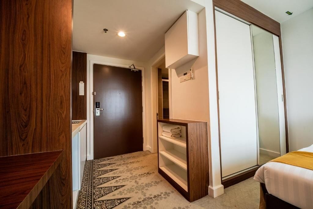 Quarto de hotel com guarda-roupa, cama, estante e tapete estampado.
