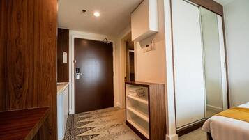 A hotel room with a wardrobe, a bed, a shelf unit, and a patterned carpet.