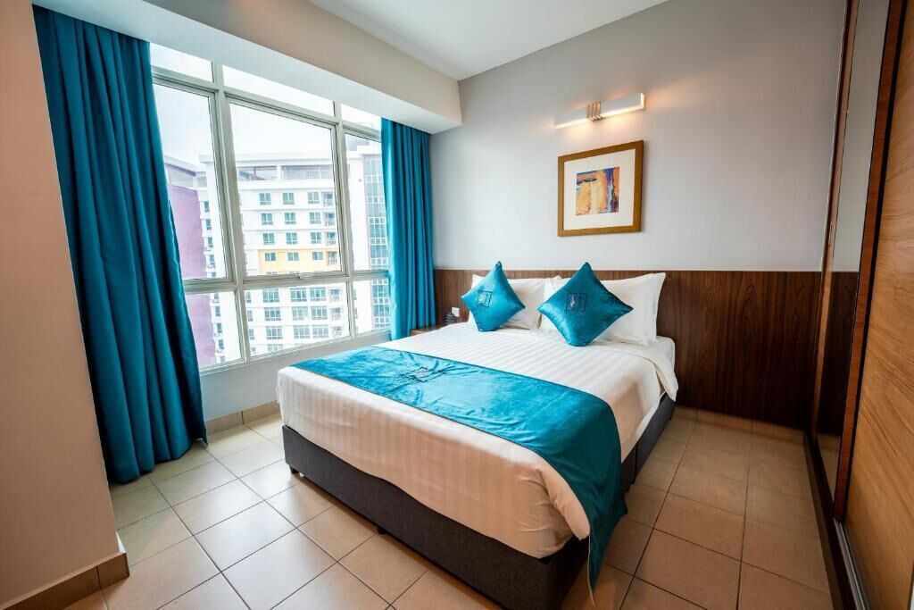 A hotel room with a bed, a window with curtains, a wall-mounted light, and a framed picture.