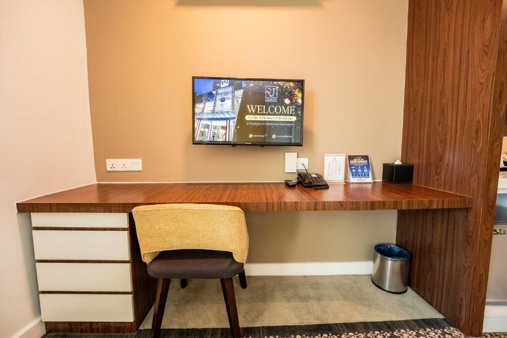 Bancada de recepção de hotel com uma televisão exibindo uma mensagem de boas-vindas, um telefone e uma lixeira.