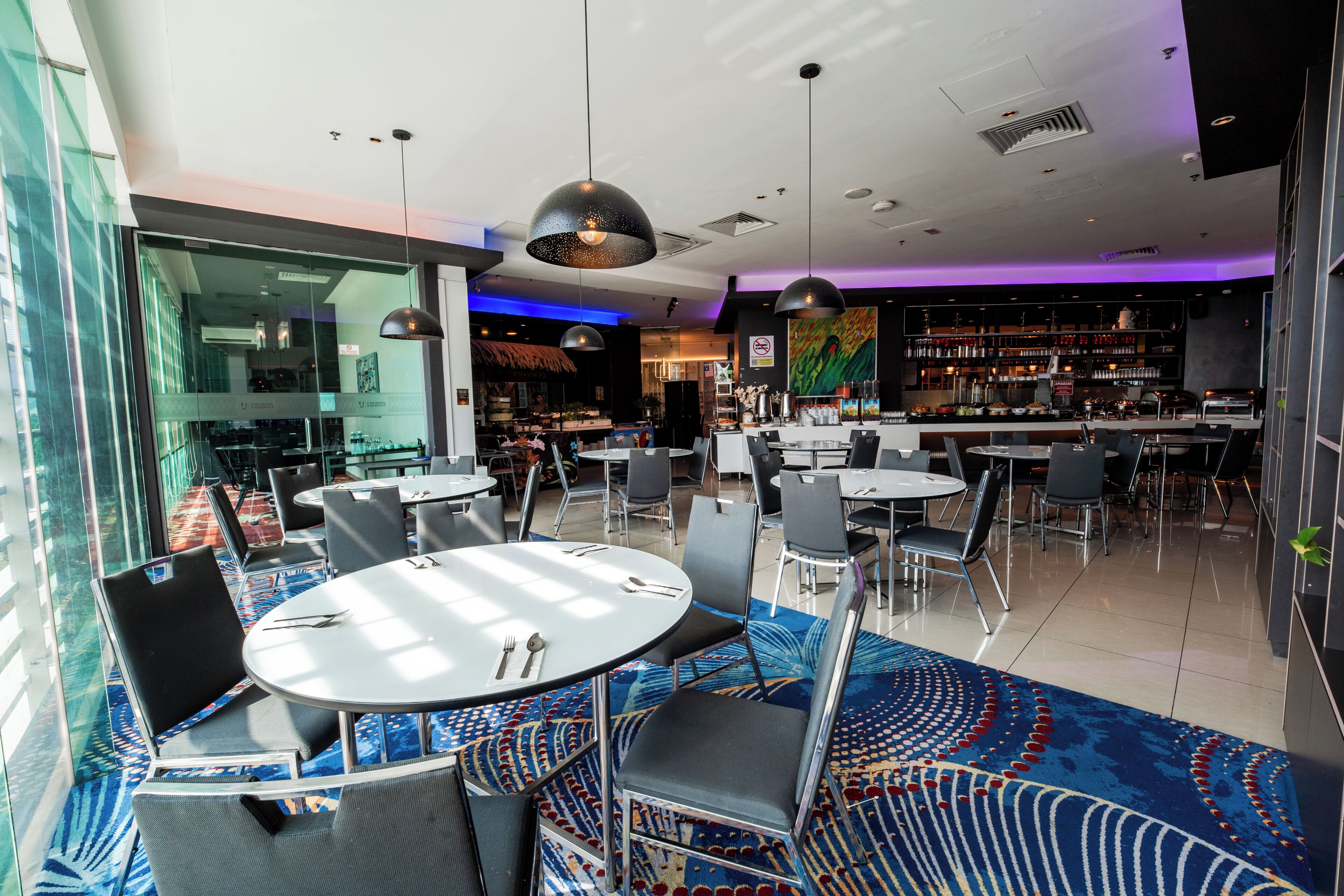 Un restaurant moderne avec des tables et des chaises rondes, un bar et une vue sur la ville grâce à de grandes fenêtres.