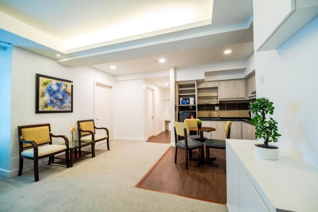 A modern living room with a sofa set, a dining table with chairs, a small kitchen area, and a potted plant.