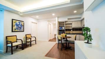 A modern living room with a sofa set, a dining table with chairs, a small kitchen area, and a potted plant.