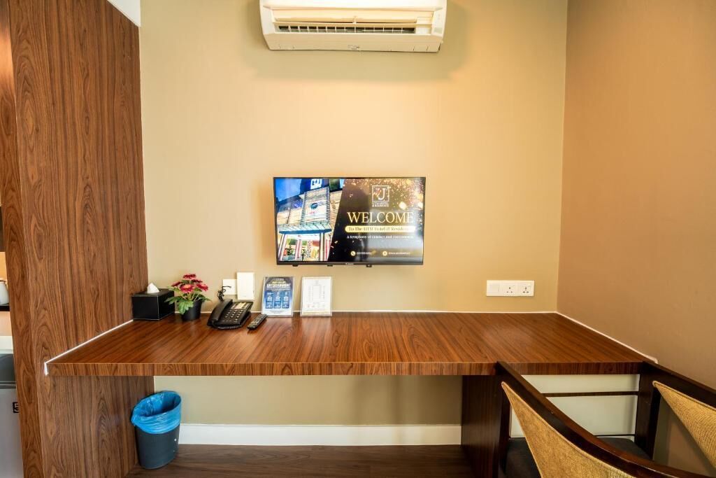 Un mostrador de recepción con televisor, un cartel de bienvenida, un teléfono y un cubo de basura.