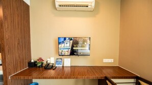 Un mostrador de recepción con televisor, un cartel de bienvenida, un teléfono y un cubo de basura.