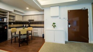 A modern kitchen with built-in cabinets, a dining area with two chairs, a small potted plant, and a brown door. - Utm Hotel Residence (Kuala Lumpur)
