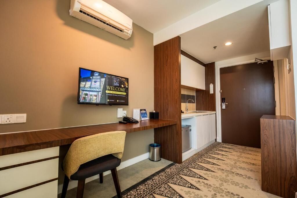 A reception area with a wooden desk, a chair, a television displaying a welcome message, and a patterned carpet.