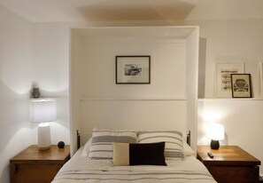 A bedroom with a bed, two bedside tables, a nightstand, a lamp, a framed picture on the wall, and a framed advertisement on the wall. - Welcoming 1-bedroom studio in Anchorage perfect for your getaway (Anchorage)