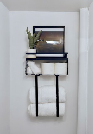 A wall-mounted shelf with a framed picture, a potted plant, and folded towels. - Welcoming 1-bedroom studio in Anchorage perfect for your getaway (Anchorage)