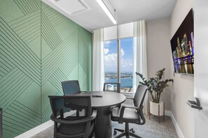 Ein moderner Büroraum mit großem Fenster und Blick auf die Stadt, einer Wand mit grünem Muster und einer Zimmerpflanze.
