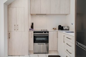 A compact kitchen with a built-in oven, a coffee maker, and a toaster. - Modern Te Atatu Sanctuary | Air-con and Sofa Bed (Auckland West)