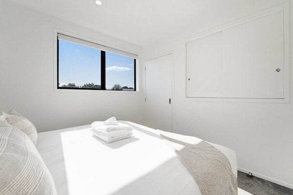 A hotel room with a large bed, a window with a view, a door, and a white wall.
