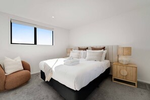 Ein Schlafzimmer mit einem Bett, Nachttischen, einem Sessel und einem Fenster.