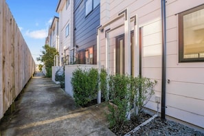 A narrow pathway between two modern buildings with a concrete floor and small plants.
