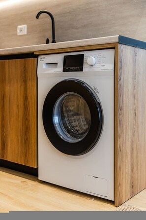 A front view of a modern washing machine with a control panel, set in a wooden cabinet with a countertop above. - Olive House Modern Escape (Tirana)