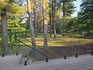 A wooden deck with a glass balustrade overlooking a grassy area with trees. - Luxury Modern Cottage | 4 Ensuite Bedrooms | Sleeps 10 | Near Lake (Sundridge)