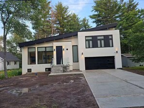 Ein modernes, zweistöckiges Haus mit Garage, großen Fenstern und einer Betonauffahrt.