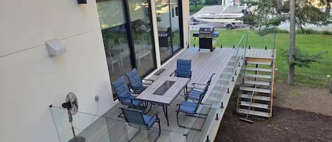 En overdækket terrasse med et bord, stole, ventilator og grill.