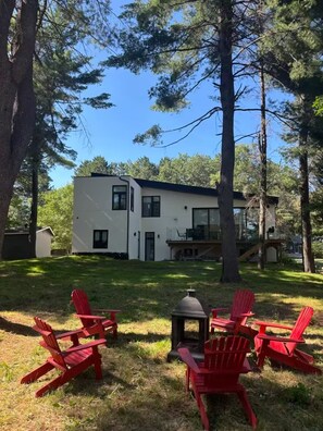 Ein modernes Haus mit Terrasse, umgeben von Bäumen, und roten Adirondack-Stühlen im Garten.