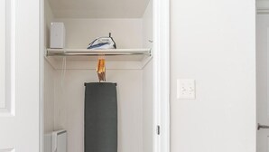 Un mur blanc sur lequel est fixée une étagère. Sur cette étagère, on peut voir une boîte blanche et un appareil bleu, ainsi qu’un objet cylindrique noir et une prise électrique blanche.