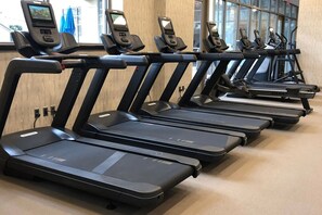 En række løbebånd i et fitnesscenter med en trævæg og vinduer i baggrunden.
