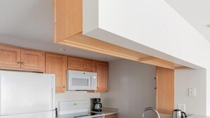 Une cuisine moderne avec des meubles en bois, un réfrigérateur blanc, un four à micro-ondes, une cuisinière et une machine à café.