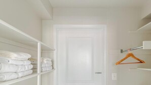 Un placard blanc, doté d’étagères et d’une porte, contenant des serviettes pliées et un cintre en bois.