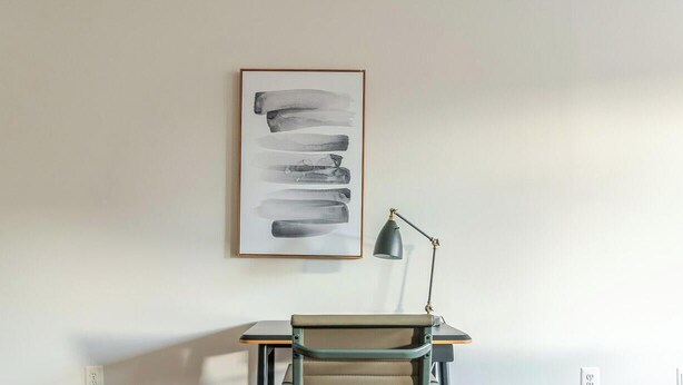 Une pièce au décor minimaliste, avec un bureau, une chaise et un tableau abstrait encadré accroché au mur.