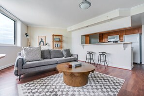 Ein modernes Wohnzimmer mit einem grauen Sofa, einem runden Holztisch und einem karierten Teppich.