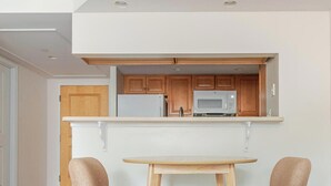 Une cuisine compacte avec des meubles en bois, un réfrigérateur blanc, un four à micro-ondes et une petite table à manger avec deux chaises.